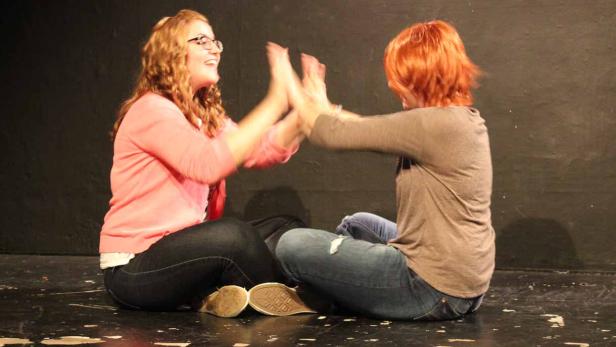 Zwei Frauen sitzen einander gegenüber und klatschen in die Hände.