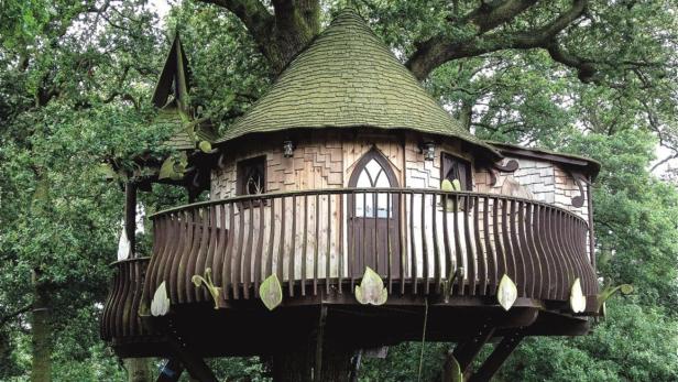 Ein Baumhaus mit einem kegelförmigen Dach inmitten von dichtem Grün.