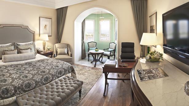 Ein luxuriöses Hotelzimmer mit einem Bett, einem Schreibtisch und einem Erker mit Sitzgelegenheit.