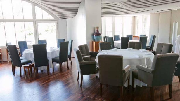 Ein Speisesaal mit runden Tischen und Stühlen unter einer dekorativen Decke.