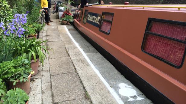 Ein Kanalboot namens „Gladstone“ liegt an einem von Blumen gesäumten Ufer.