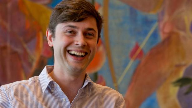 Ein lachender junger Mann vor einem bunten Gemälde.