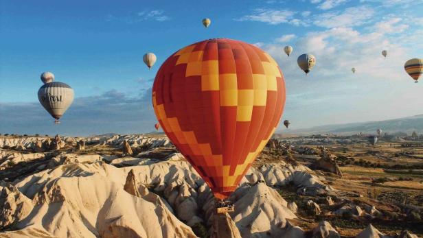 Mehrere Heißluftballons schweben über einer zerklüfteten Landschaft in Kappadokien.
