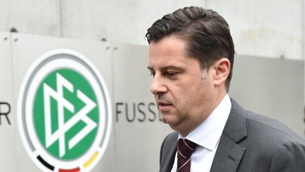 Ein Mann in Anzug steht vor dem Logo des Deutschen Fußball-Bundes (DFB).