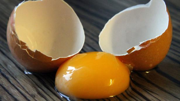 Ein aufgeschlagenes Ei mit Eigelb und Eierschalen auf einer Holzoberfläche.