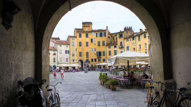 Blick durch einen Torbogen auf einen belebten Platz in Lucca, Italien.
