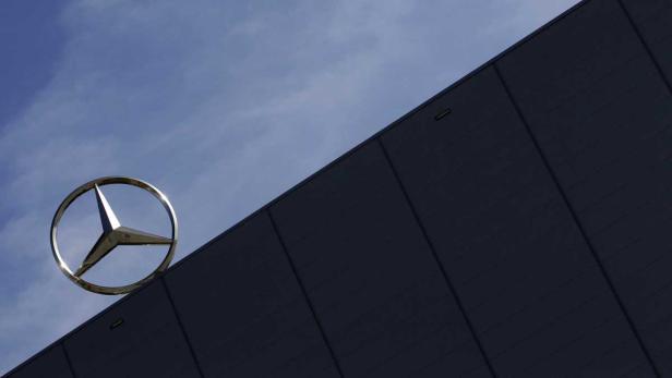 Das Mercedes-Benz-Logo vor einem blauen Himmel und einer dunklen Gebäudefassade.