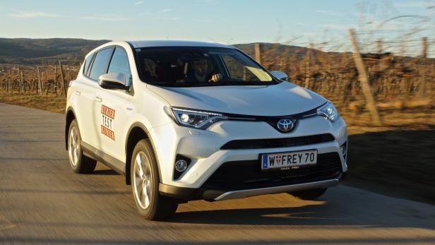 Ein weißer Toyota RAV4 fährt auf einer Straße durch eine ländliche Gegend.
