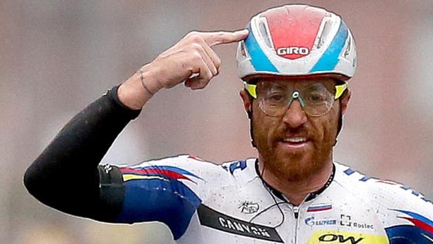 Ein Radrennfahrer mit Brille und Helm deutet auf seinen Kopf.