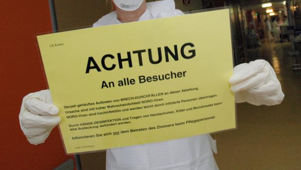 Eine Person im Krankenhaus hält ein Schild mit der Aufschrift „Achtung An alle Besucher“.