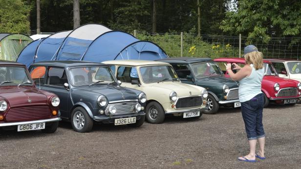 Eine Frau fotografiert eine Reihe von klassischen Mini Cooper Autos vor Zelten.