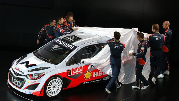 Mehrere Teammitglieder enthüllen einen Hyundai i20 WRC Rallyewagen.