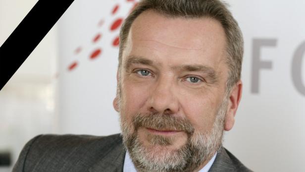 Porträt eines Mannes mit Bart und Anzug vor einem hellen Hintergrund.