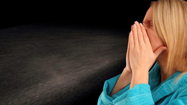 Eine Frau im Bademantel hält sich die Hände vor das Gesicht, während sie hustet oder niest.