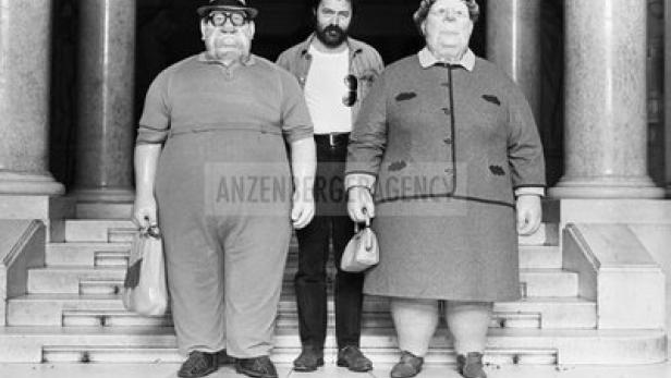Manfred Deix vor der Hofburg mit zwei österreichischen Figuren.
