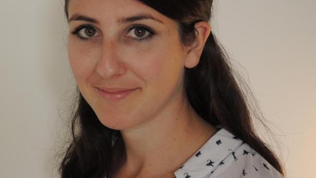 Eine Frau mit dunklen Haaren und einem Hemd mit Katzenmuster lächelt.