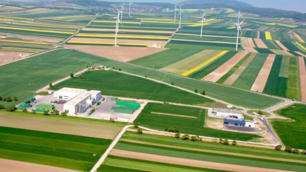 Luftaufnahme einer ländlichen Gegend mit Feldern, Windrädern und einem Industriegebiet.