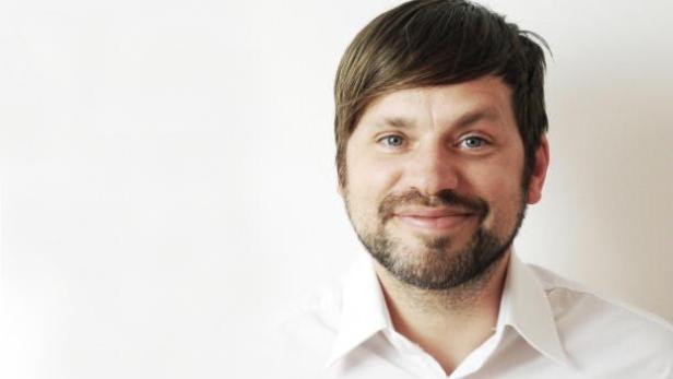 Ein Mann mit Bart und blauem Hemd lächelt in die Kamera.