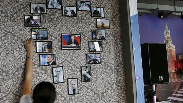 Eine Frau hängt Fotos von Wladimir Putin an eine gemusterte Wand.