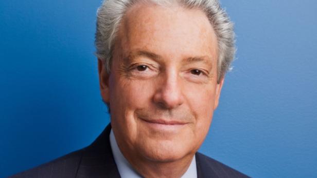 Porträt eines älteren Mannes mit grauem Haar vor einem blauen Hintergrund.