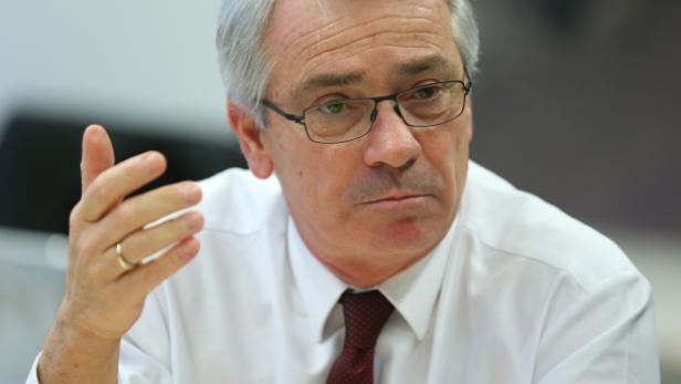 Ein Mann mit Brille, weißem Hemd und Krawatte gestikuliert mit der Hand.