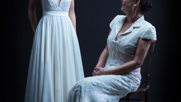 Zwei Frauen in weißen Kleidern posieren vor einem dunklen Hintergrund.