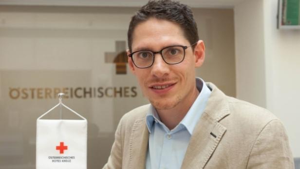 Ein Mann mit Brille und hellem Sakko vor dem Hintergrund des Österreichischen Roten Kreuzes.