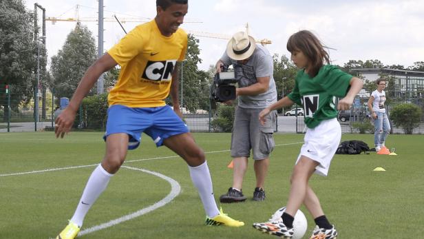Zwei Kinder spielen Fußball, während ein Kameramann die Szene filmt.