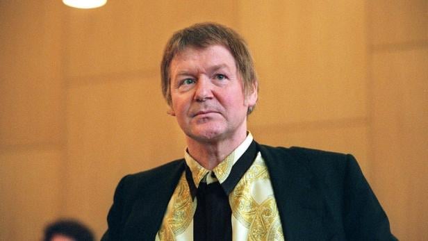 Ein Mann mit gemustertem Hemd und dunklem Sakko blickt nachdenklich.