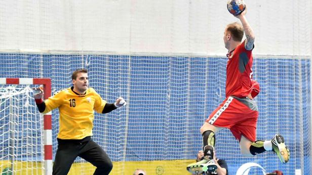 Ein Handballspieler springt, um einen Ball auf das Tor zu werfen, während der Torwart versucht, ihn abzuwehren.