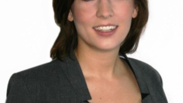 Eine Frau mit braunen Haaren und einem grauen Blazer lächelt.