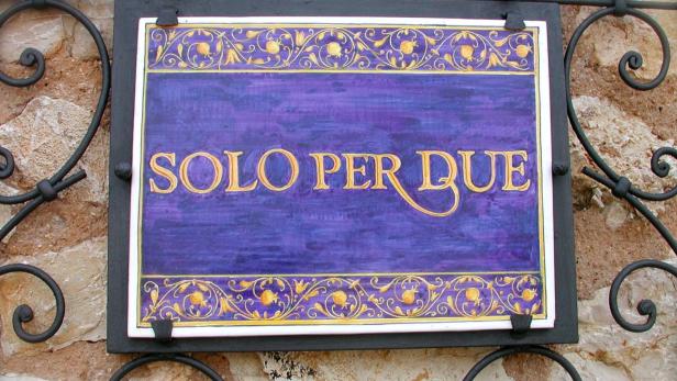 Ein Schild mit der Aufschrift „Solo per Due“ hängt an einer verzierten Halterung.