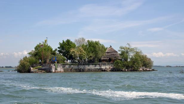 Eine kleine Insel mit einem strohgedeckten Haus im flachen Wasser.