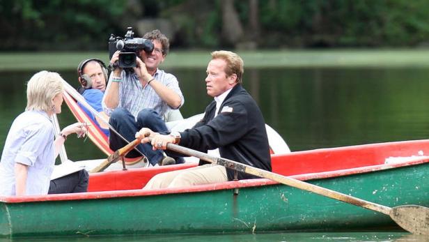 Arnold Schwarzenegger rudert in einem Boot, während er von einem Kamerateam gefilmt wird.