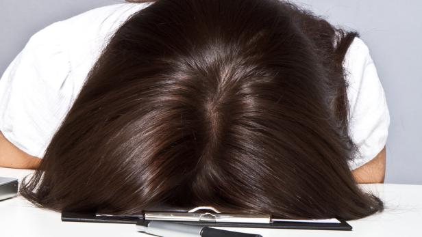 Eine Frau liegt erschöpft mit dem Kopf auf einem Schreibtisch.