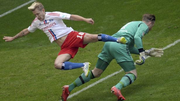 Ein Fußballspieler grätscht nach dem Ball, während ein Torwart versucht, ihn abzuwehren.