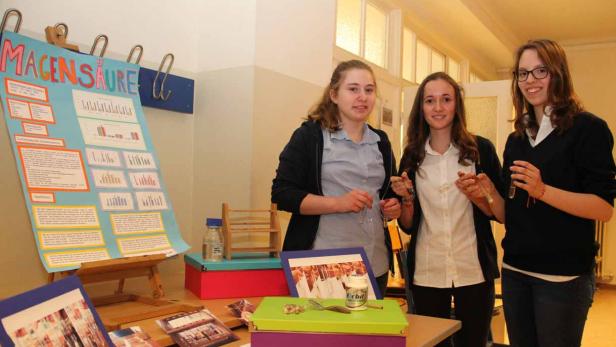 Drei Schülerinnen präsentieren ein Projekt zum Thema Magensäure mit Postern und Experimenten.