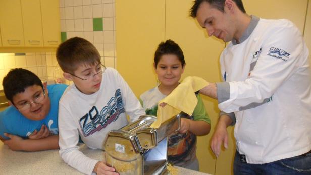 Ein Koch zeigt einer Gruppe von Kindern, wie man mit einer Nudelmaschine Pasta herstellt.
