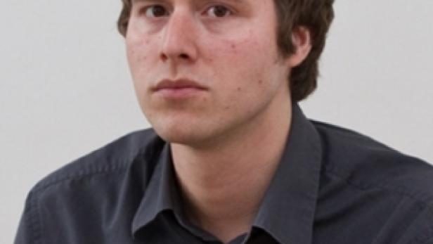 Ein Porträt eines jungen Mannes mit braunen Haaren und einem grauen Hemd.