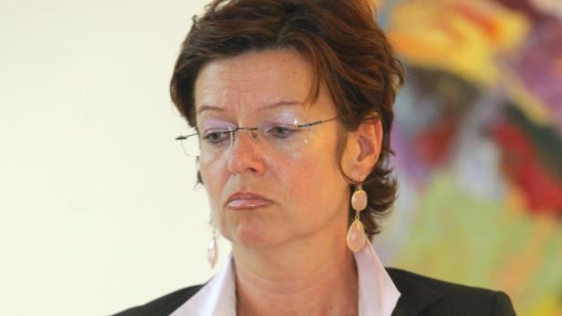 Eine Frau mit Brille und Ohrringen blickt nachdenklich zur Seite.