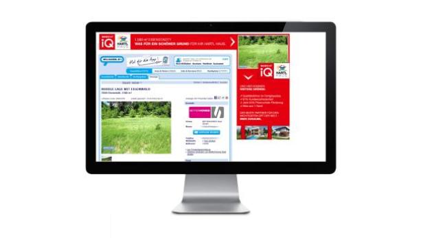 Ein Computermonitor zeigt eine Webseite für Hartl Haus mit einem Grundstücksangebot.