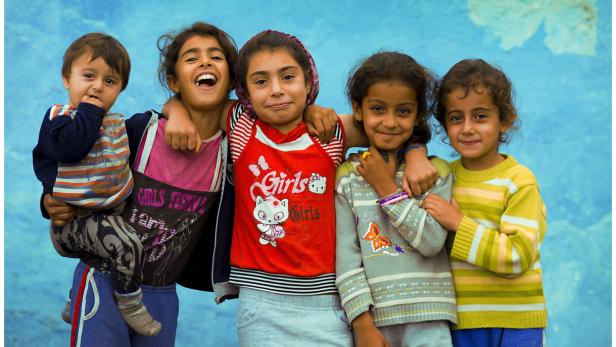Fünf lächelnde Kinder stehen vor einer blauen Wand.