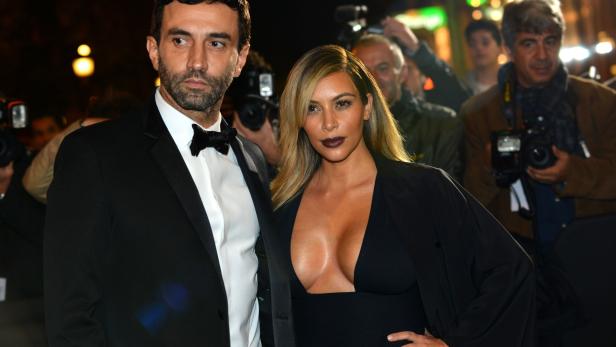 Kim Kardashian posiert mit einem Mann im Anzug auf einem roten Teppich.