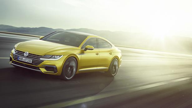 Ein gelber Volkswagen Arteon fährt auf einer Straße mit Bergen im Hintergrund.