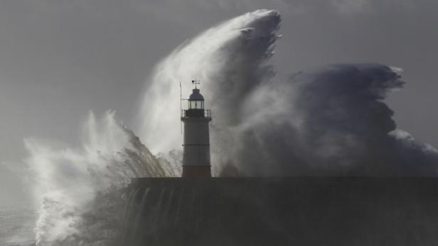 Eine riesige Welle bricht an einem Leuchtturm an einer Mole.