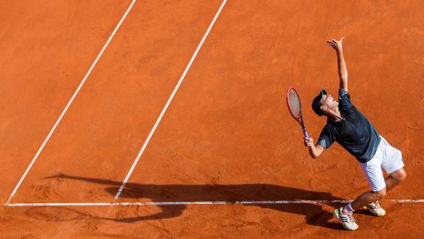 Ein Tennisspieler serviert auf einem roten Sandplatz.