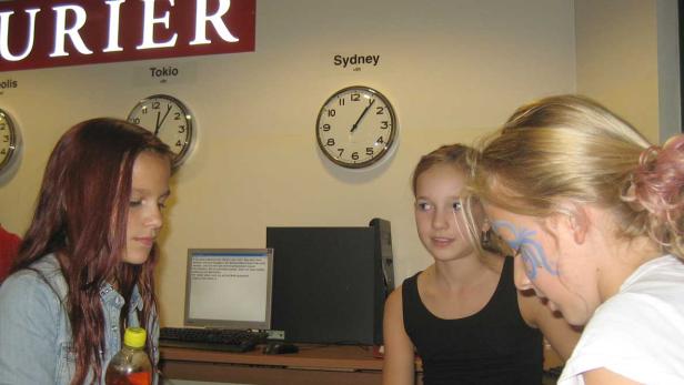 Drei Mädchen stehen vor einer Wand mit Uhren, die verschiedene Zeitzonen anzeigen.