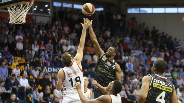 Zwei Basketballspieler kämpfen um den Ball vor einer Zuschauertribüne.