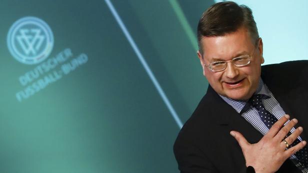 Ein Mann in Anzug steht vor einem Hintergrund des Deutschen Fußball-Bundes.