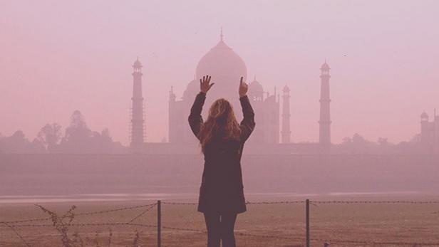 Eine Frau steht mit erhobenen Armen vor dem Taj Mahal im Nebel.